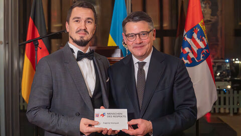 Ministerpräsident Boris Rhein und Evgenij Voznyuk stehen vor Deutschlandflagge, Ukraine-Flagge und Hessen-Flagge. Beide halten Auszeichnung mit dem Logo "Menschen des Respekts"