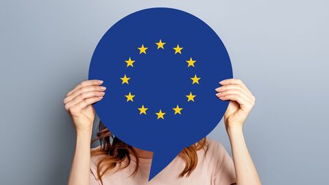Auf dem Foto ist die obere Hälfte einer Frau zu sehen, die sich eine Sprechblase im EU-Design vor das Gesicht hält, sodass dieses nicht mehr zu sehen ist.