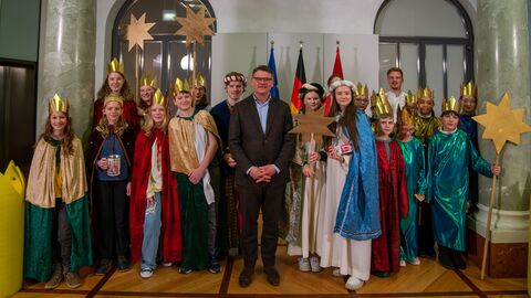 Ministerpräsident Boris Rhein steht gemeinsam mit einer Gruppe Kindern in Sternsinger-Kostümen in einem Raum der Staatskanzlei.