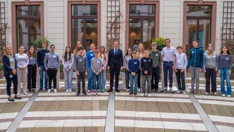 Schülerinnen und Schüler stehen nebeneinander. In der Mitte steht der Chef der Staatskanzlei, Benedikt Kuhn.