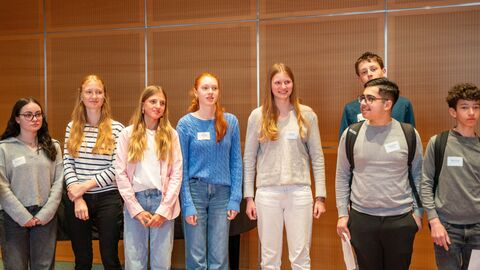 Schülerinnen und Schüler stehen nebeneinander und schauen interessiert in eine Richtung.