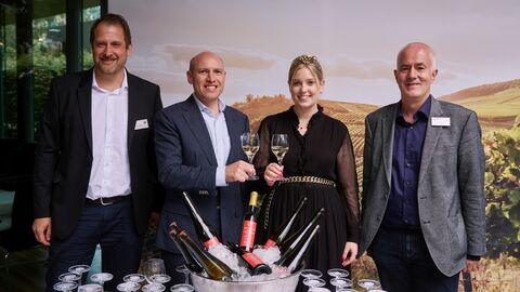 Bei der diesjährigen Weinprobe wurde erstmalig der Rotling 2022 verkostet, der aus Trauben vom hauseigenen Weinberg der Landesvertretung gewonnen wird. Die fachkundigen Mitarbeiter Christoph Donig (l.) und Christoph Wollseifer (r.) schenkten den Rotling aus Menschen lächeln in die Kamra, davor auf dem Tisch ein Weinkühler mit vielen Weinflaschen die auf Eis liegen