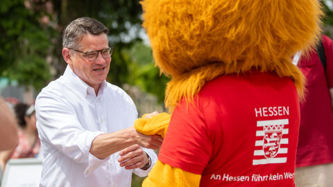 Ministerpräsident Rhein mit dem Hessen-Löwen. Ministerpräsident Rhein schüttelt dem Löwen-Maskottchen des Landes die Hand.