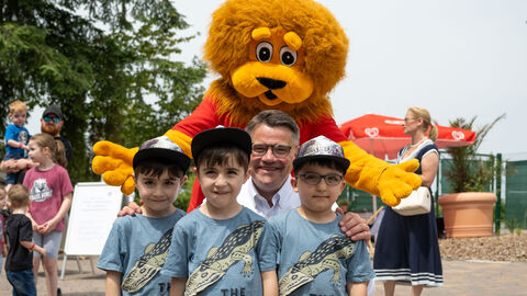 Ministerpräsident Rhein mit den Drillings-Jungen und dem Maskottchen. Ministerpräsident Rhein mit drei Drillings-Jungen, im Hintergrund der Hessen-Löwe als Maskottchen.