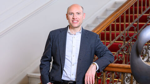 Ein Mann im blauen Anzug lehnt an einem Treppengeländer