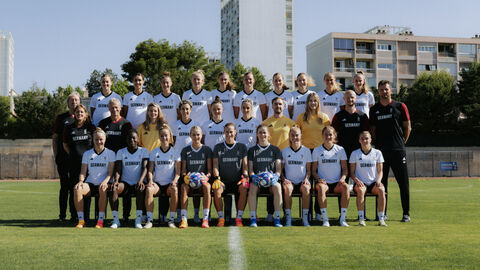Fußballerinnen in Trikots haben sich für ein Foto im Stadion aufgstellt.