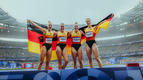 Sportlerinnen stehen auf Bühne und halten große Deutschlangflagge 