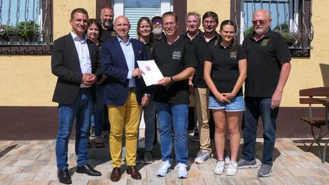 Schützenverein Smed Europaminister Pentz steht vor gelbem Haus und überreicht Mitgliedern des Schützenvereins Smed einen Förderbescheid