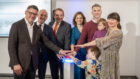 Sechs Erwachsende und zwei Kinder stehen in einem Halbkreis und strecken jeweils einen Arm in die Mitte.