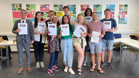 Teilnehmerinnen und Teilnehmer von Pre-College Fulda bei der Abschlussfeier Auf dem Foto sind zehn lächelnde junge Menschen in einem Klassenzimmer zu sehen, die Urkunden in der Hand halten.
