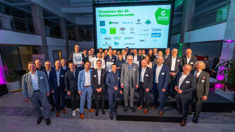 Auf dem Foto sind rund 30-40 Menschen zu sehen, hinter denen eine Leinwand mit der Aufschrift "Finalisten der 23. Wettbewerbsrunde" zu sehen ist.