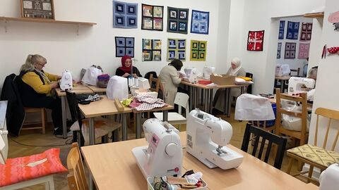 Auf dem Foto ist eine Nähstube zu sehen, in der mehrere Frauen an Nähmaschinen arbeiten.