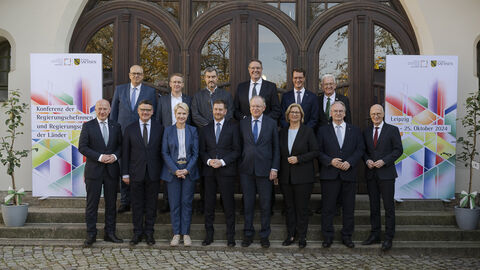 14 Männer und Frauen stehen in 2 Reihen vor einem Gebäude.