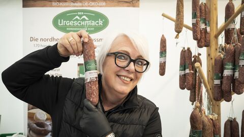 Eine Mitarbeiterin hält lächelnd eine ganze Ahle Wurscht in die Kamera