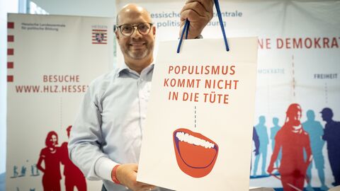 Ein Mitarbeiter hält lächelnd eine Tüte mit der Aufschrift "Populismus kommt nicht in die Tüte" in die Kamera