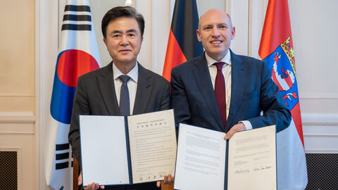 2 Männer stehen nebeneinander und halten jeweils ein Dokument in die Kamera.