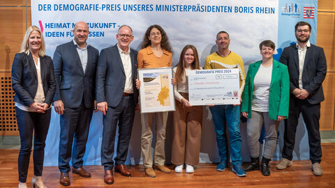 1. Preis: Kreishandwerkerschaft Odenwaldkreis, Erbach im Odenwald – Odenwälder Handwerkstage Eine Gruppe Personen steht vor einem Aufsteller mit der Aufschrift "Der Demografie-Preis unseres Ministerpräsidenten Boris Rhein". Eine Person hält eine gerahmte Urkunde in Händen, zwei weitere einen Scheck.