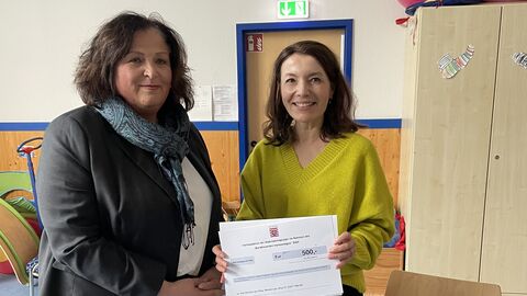 Zwei Frauen stehen nebeneinander und halten eine Urkunde hoch.