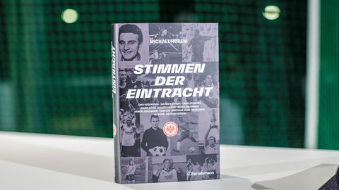 Das Buch „Stimmen der Eintracht“ (Hardcover, Schwarz-Weiß-Einband) steht auf einem weißen Tisch 