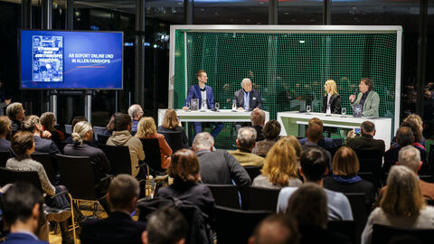 Auf dem Podium nahmen Platz (v.l.n.r.): Daniel Wolf (Stadionsprecher), Matthias Ohms (ehemaliger Eintracht-Präsident), Sabrina Wagner (Tochter von Bernd Hölzenbein) und Michael Horeni (Buchautor) Die Teilnehmer der Lesung sitzen vor dem Publikum auf der Bühne, im Hintergrund steht ein Fußballtor