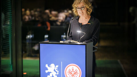 Eine Frau steht am Pult und liest den Gästen aus dem Buch vor