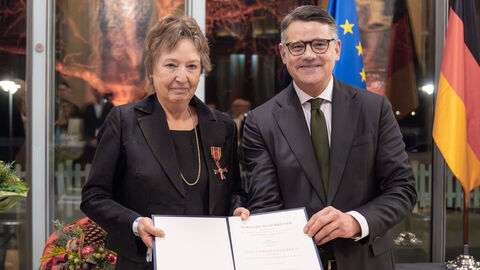 Frau und Mann blicken in Kamera und halten Urkunde in den Händen.