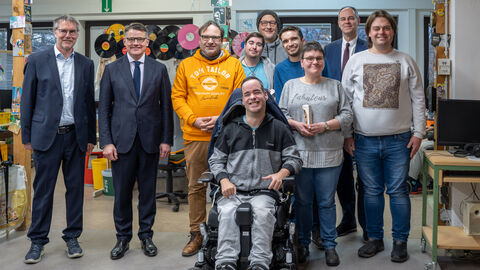 Mehrere Menschen schauen in Kamera. Eine Person sitzt im Rollstuhl