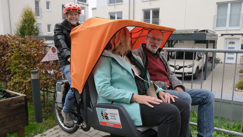 „Soziale Anlauf- und Begegnungsstätte für alle Generationen – DAS INNOVATIVE SOZIALZENTRUM“ Zwei Personen sitzen auf einer Rikscha