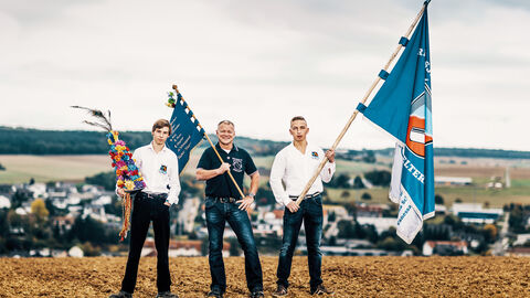 Wir für unser Dorf Drei Männer posieren mit Fahnen