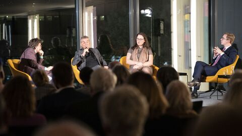 Vier Personen sitzen im Halbkreis auf Stühlen auf dem Podium und diskutieren