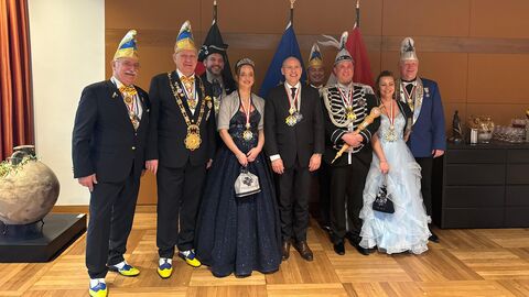 Minister Manfred Pentz steht mit dem Prinzenpaar sowie sechs weiteren festlich angezogenen Personen in einem Bürogebäude