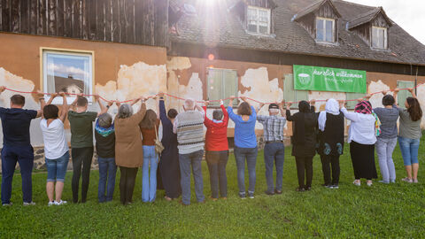 Die Mitglieder des Kulturcafé Gambach e. V. stehen vor ihrem Café, verbunden durch einen roten Faden, den sie in den Händen halten. Die Mitglieder des Kulturcafé Gambach e. V. stehen vor ihrem Café, verbunden durch einen roten Faden, den sie in den Händen halten.