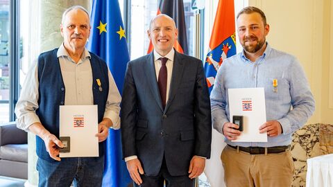 Robert Schmitt, Staatsminister Manfred Pentz und Steffen Lippert stehen nebeneinander und halten Urkunden in Händen.