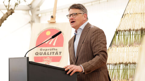 Rede Eröffnung Spargelsaison 2025 Ministerpräsident Rhein steht an einem Rednerpult und spricht. im Hintergrund ist ein Aufsteller mit Spargel zu sehen und ein Aufsteller "Geprüfte Qualität" mit dem Hessenlöwen.