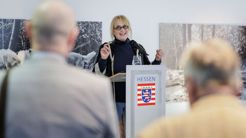 Die Fotografin Ruth Marcus begrüßt Gäste zur Vernissage in der HLV Berlin