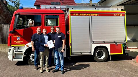 Vier Männer stehen vor Feuerwehrauto.