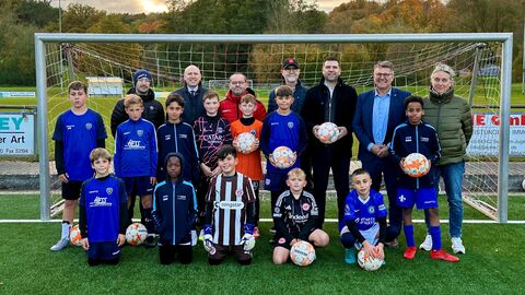 Eine Gruppe von jungen Fußballern sowie sieben erwachsene stehen auf einem Kunstrasenplatz vor einem Fußballtor