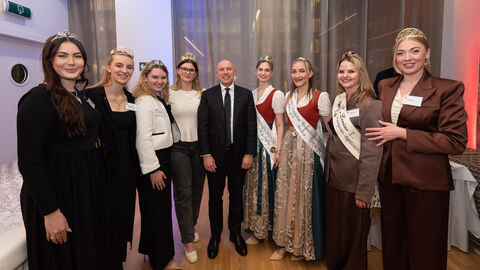 Acht Frauen stehen in festlicher Robe nebeneinander. In der Mitte steht ein Mann im Anzug.