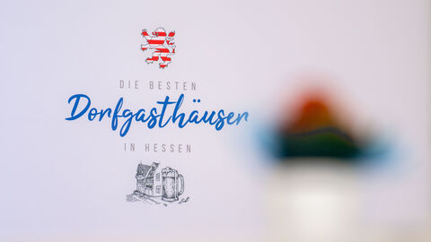 Nahaufnahme von einem weißen Aufsteller. Darauf steht geschrieben "Die Besten Dorfgasthäuser in Hessen".
