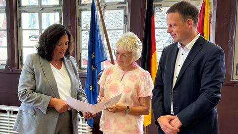 Drei Personen stehen nebeneinander und schauen auf eine Urkunde.