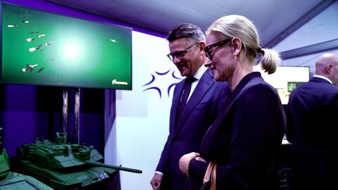 Ministerpräsident Rhein steht mit einer Frau vor einem Miniaturpanzer