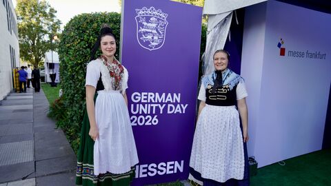 Zwei Frauen in Tracht stehen neben einem Aufsteller "German Unity Day 2026"