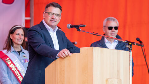 Ministerpräsident Rhein am Rednerpult bei der Spargelwanderung, hinter ihm die Lampertheimer Spargelprinzessin.