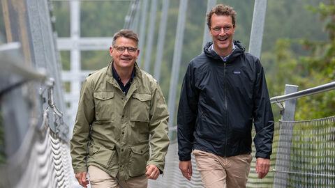 Hessens Ministerpräsident Boris Rhein und Nordrhein-Westfalens Ministerpräsident Hendrik Wüst wanderten gemeinsam vom nordhessischen Willingen ins südwestfälische Winterberg und besuchten dabei in der Nähe von Willingen die längste Hängebrücke Deutschlands, den „Skywalk“. Hessens Ministerpräsident Boris Rhein (links) und Nordrhein-Westfalens Ministerpräsident Hendrik Wüst (rechts) in der Nähe von Willingen auf der längsten Hängebrücke Deutschlands, dem „Skywalk“, auf die Kamera zulaufend