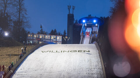 Skispringer springt von Schanze mit einem Schriftzug "Willingen" bei Nacht
