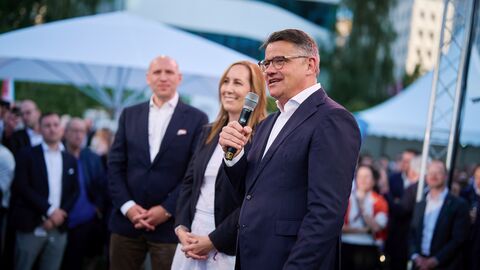 Ministerpräsident Rhein steht gemeinsam mit Landtagspräsidentin Astrid Wallmann und Europaminister Pentz vor Publikum und spricht ins Mikrofon.