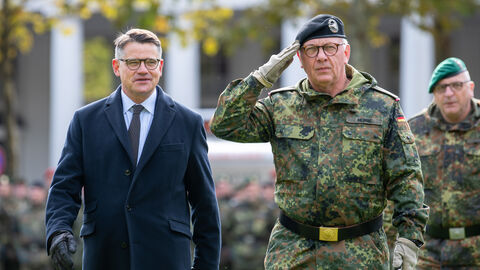 Ministerpräsident Rhein steht neben einem Bundeswehr-Soldaten, der salutiert