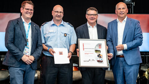 Mehrere Personen stehen nebeneinander auf einer Bühne und halten eine Urkunde 