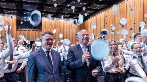 Ministerpräsident Boris Rhein und Innenminister Roman Poseck stehen inmitten von Mneschen, die ihre Mützen in die Luft werfen. 