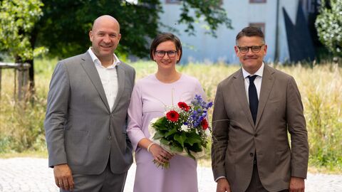 Zwei Männer und ne Frau lachen in Kamera. die Frau hält einen Blumenstrauß.
